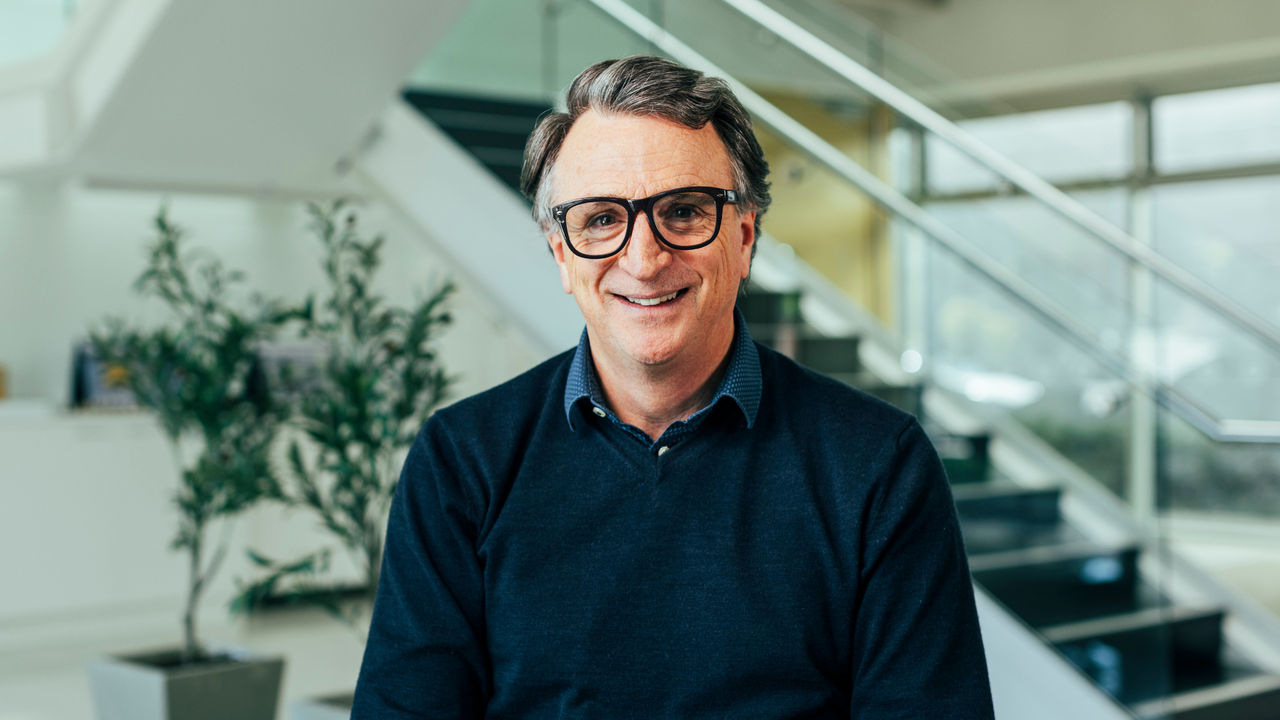 Image of Sean Whitaker, Project Management Consultant in front of office scene with stairs and indoor plants in background.