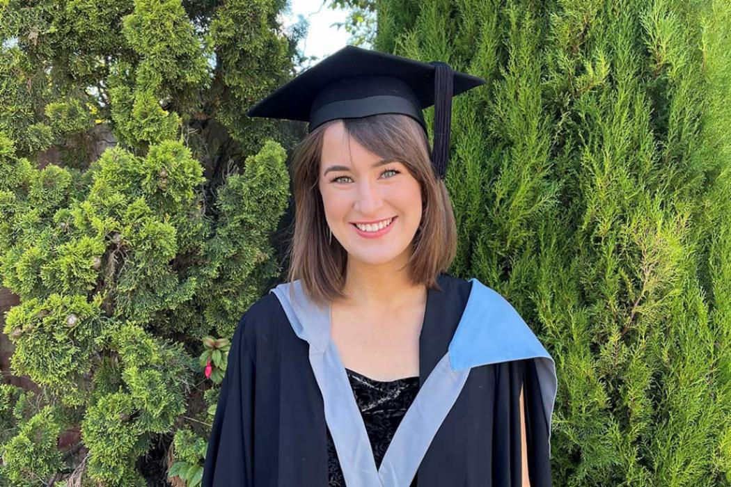 A smiling student, sitting at a desk with her laptop, makes a phone call to the UC Online learner support team.