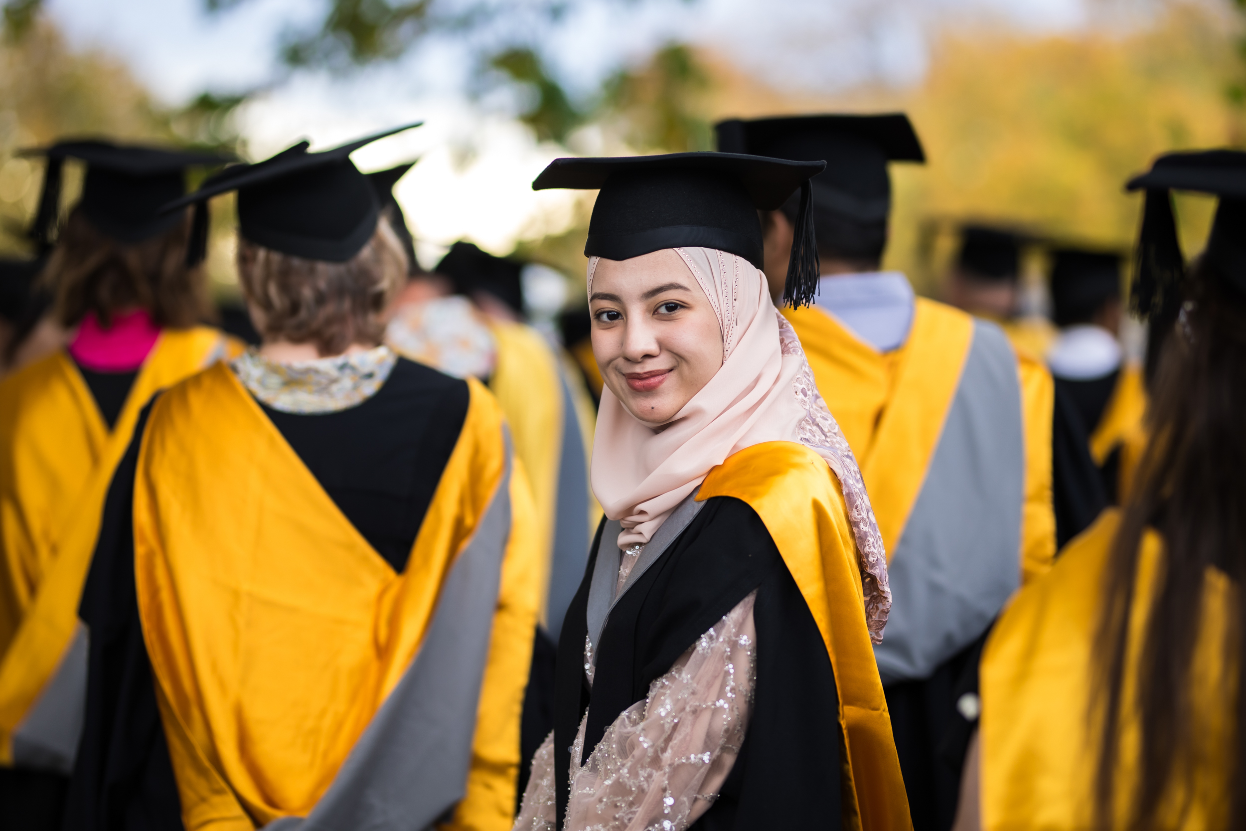 A UC student wearing graduation regalia robe, cap, and hood with the Business gold colour.
