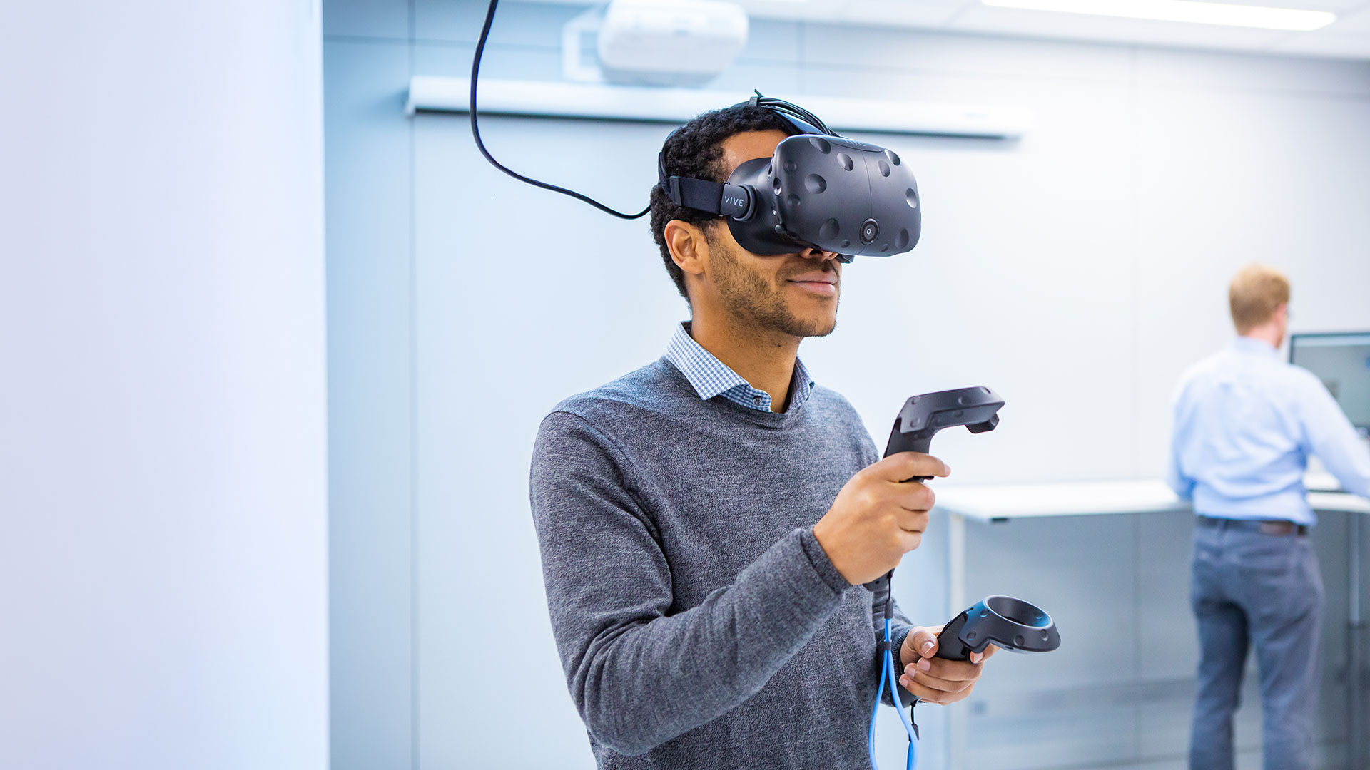 Person in computer lab wearing a virtual reality headset and holding controllers