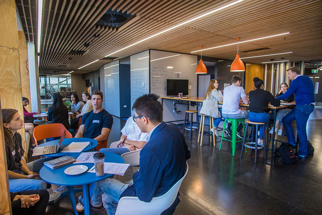 Groups of UC Business students sitting at different tables in the Rehua building during a mentoring event.