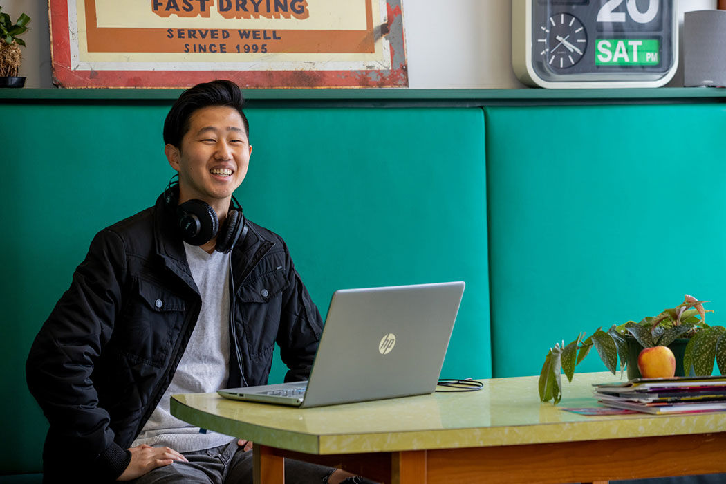 Smiling student sitting at a booth in a café with a latop.