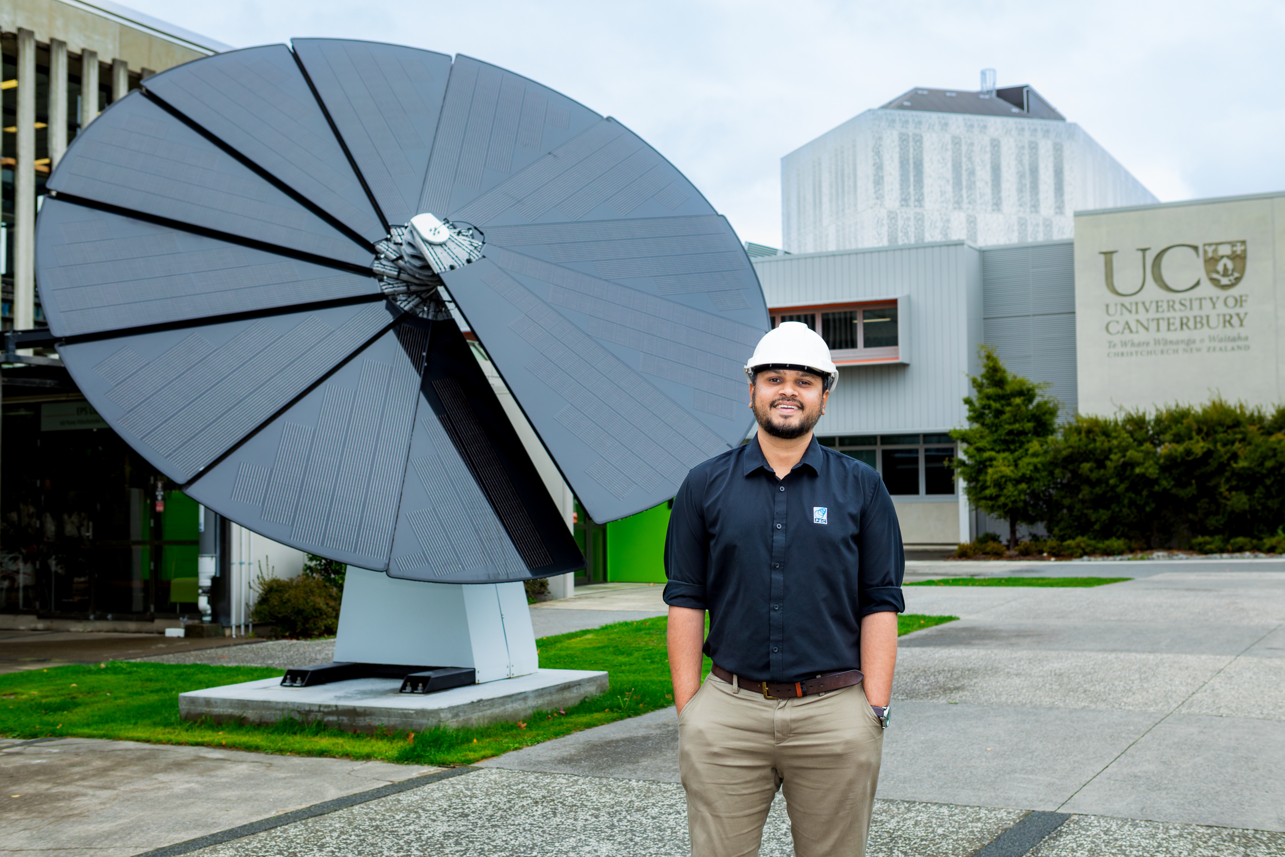 A UC engineer stands in front of the 5 metre tall 'Solar Sunflower' solar panel scultpure on the lawn outside of the Rehua building.