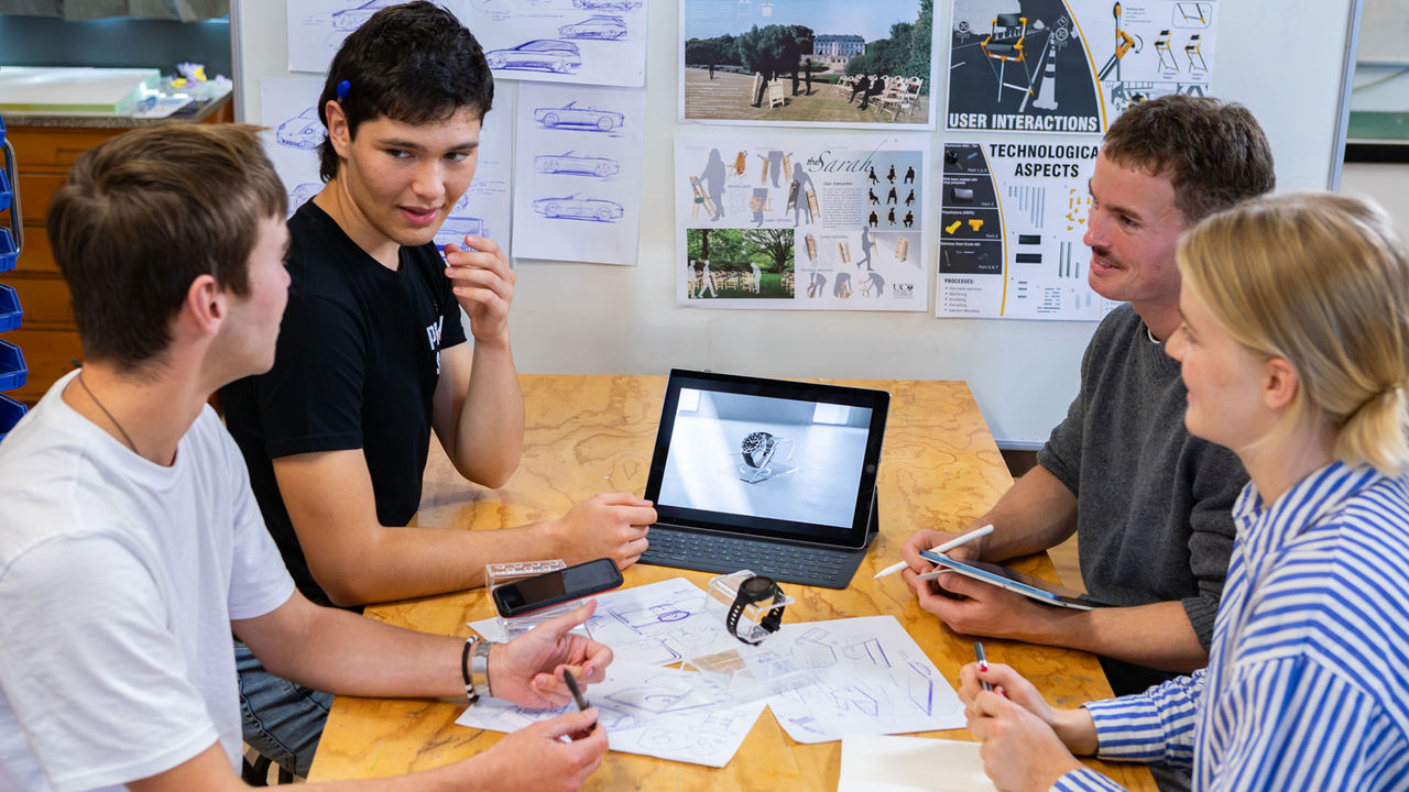 Industrial Product design students working at a table together with design sketches.