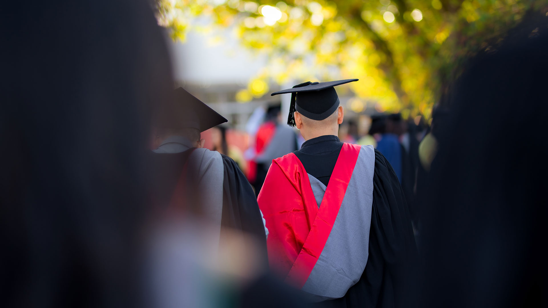 UC graduation student wearing graduation regalia and a red hood for their Social Work degree.