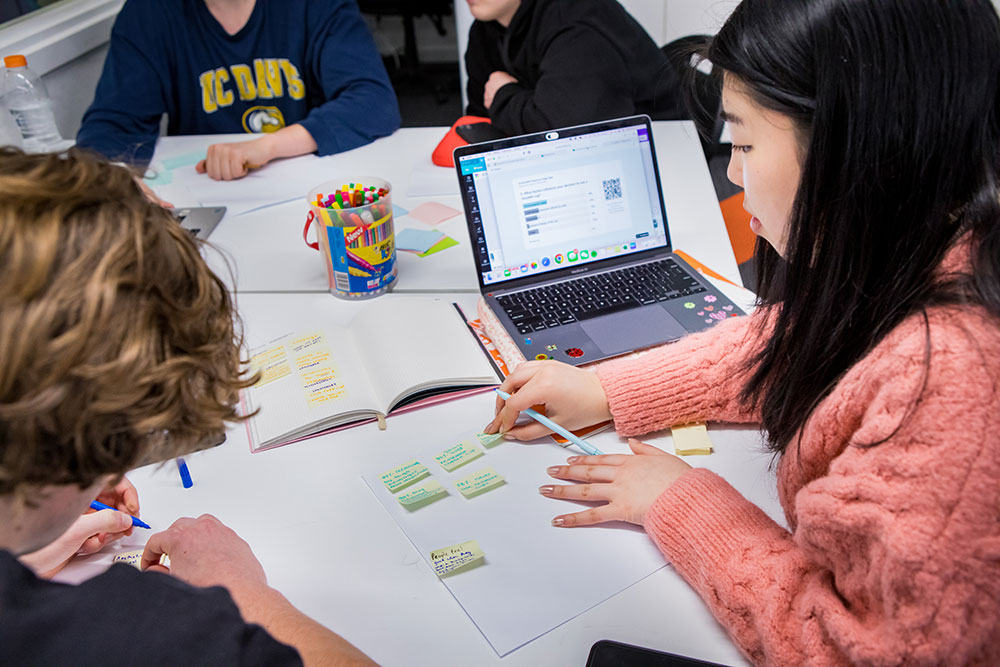 UC students gathered around a table writing ideas on post-it notes.