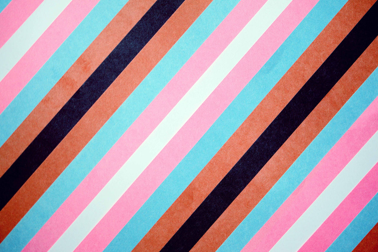 Repeating strips of paper arranged diagonally down from the top left corner to the bottom right corner. In colour order; black, brown, white, pink, light blue to represent the transgender and BIPOC communities.