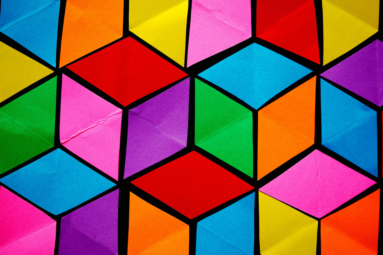 Multiple bright coloured paper diamonds arranged to create a 3D cube pattern