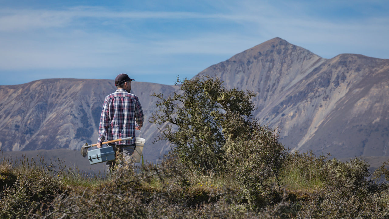 Student in the field carrying a shovel with mountains in the background