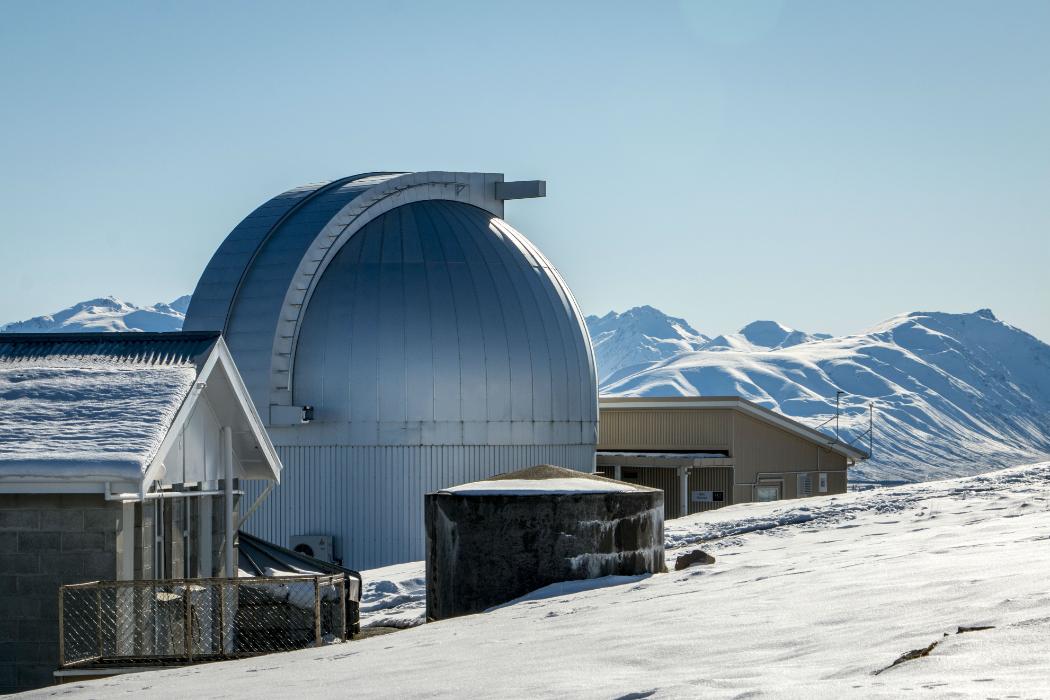Exterior of Mt John Observatory on a sunny day in winter, with snowy mountains in the distance.