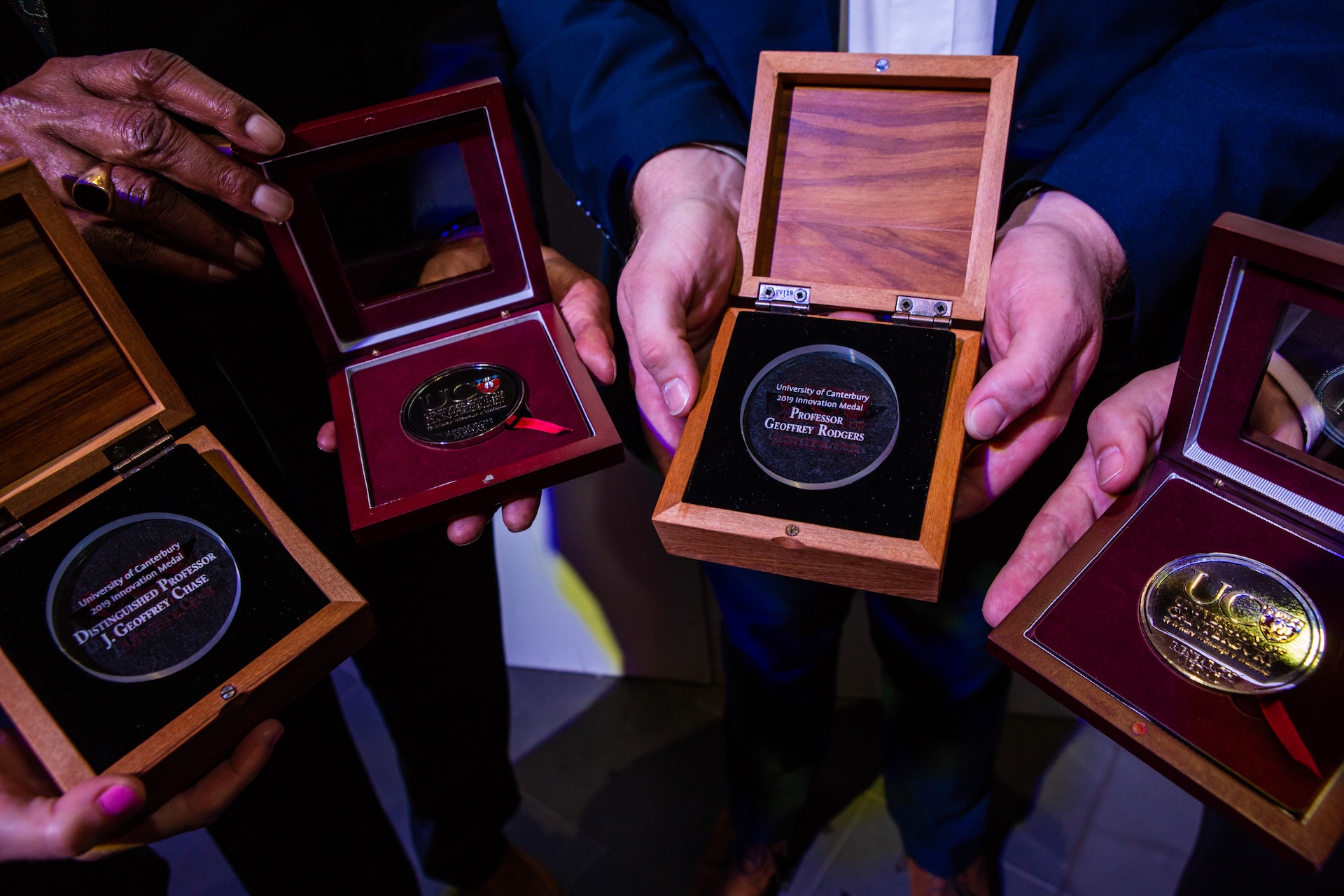 Four UC medals in wooden cases being held in a circle.