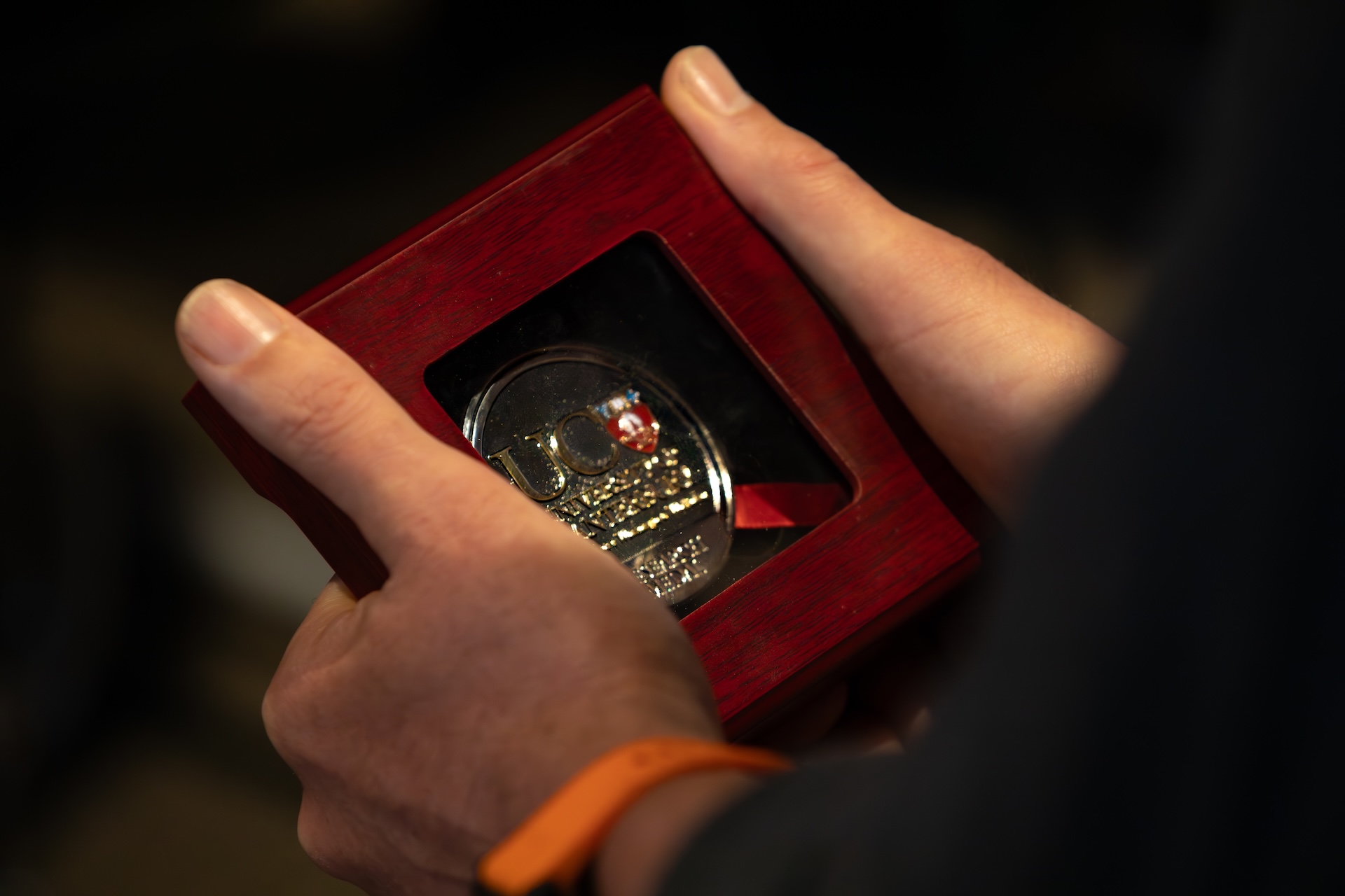 Person's hands holding a gold medal with a UC logo in a wooden case.