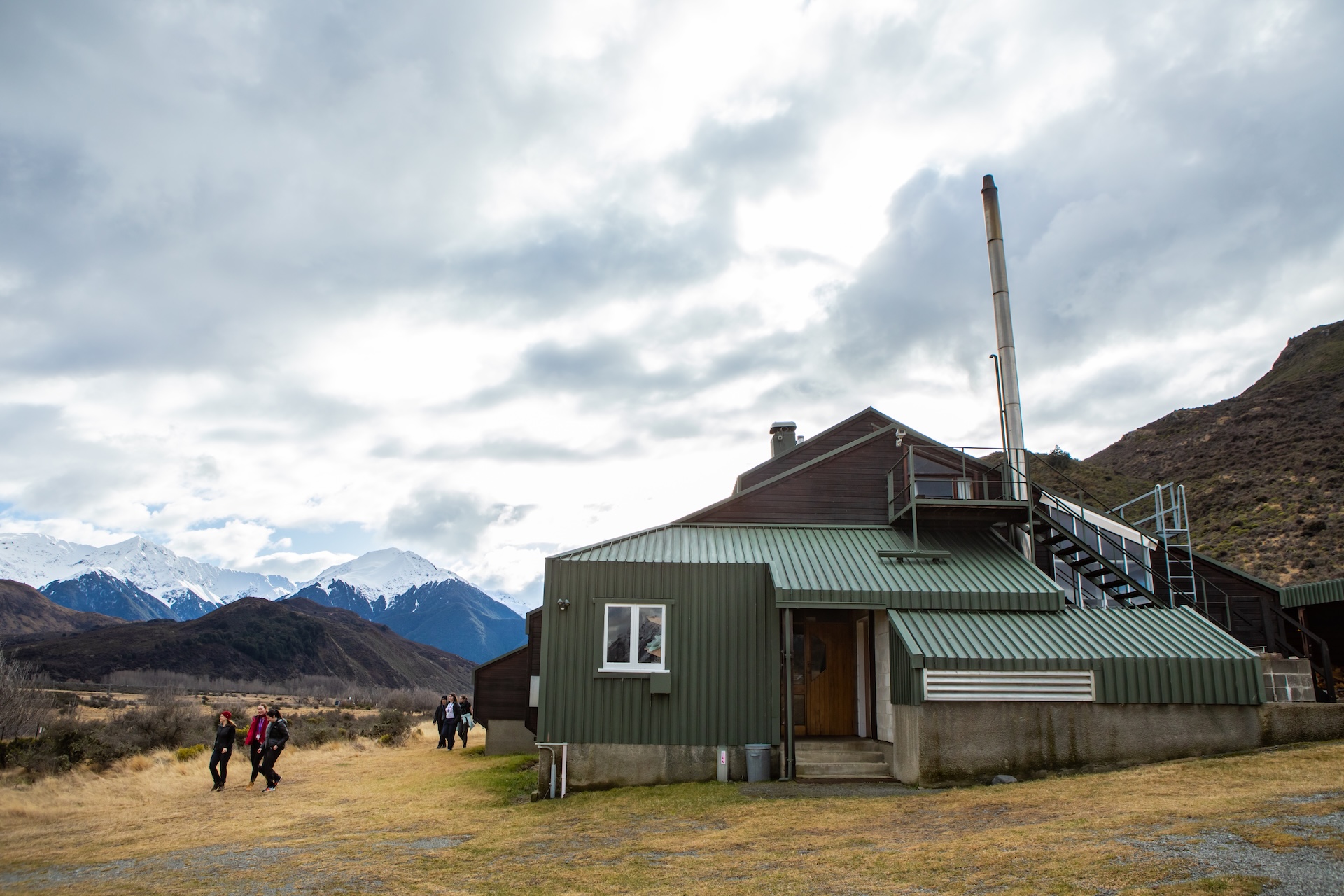 Station building surrounded by tussocks, hills and snowy mountains.