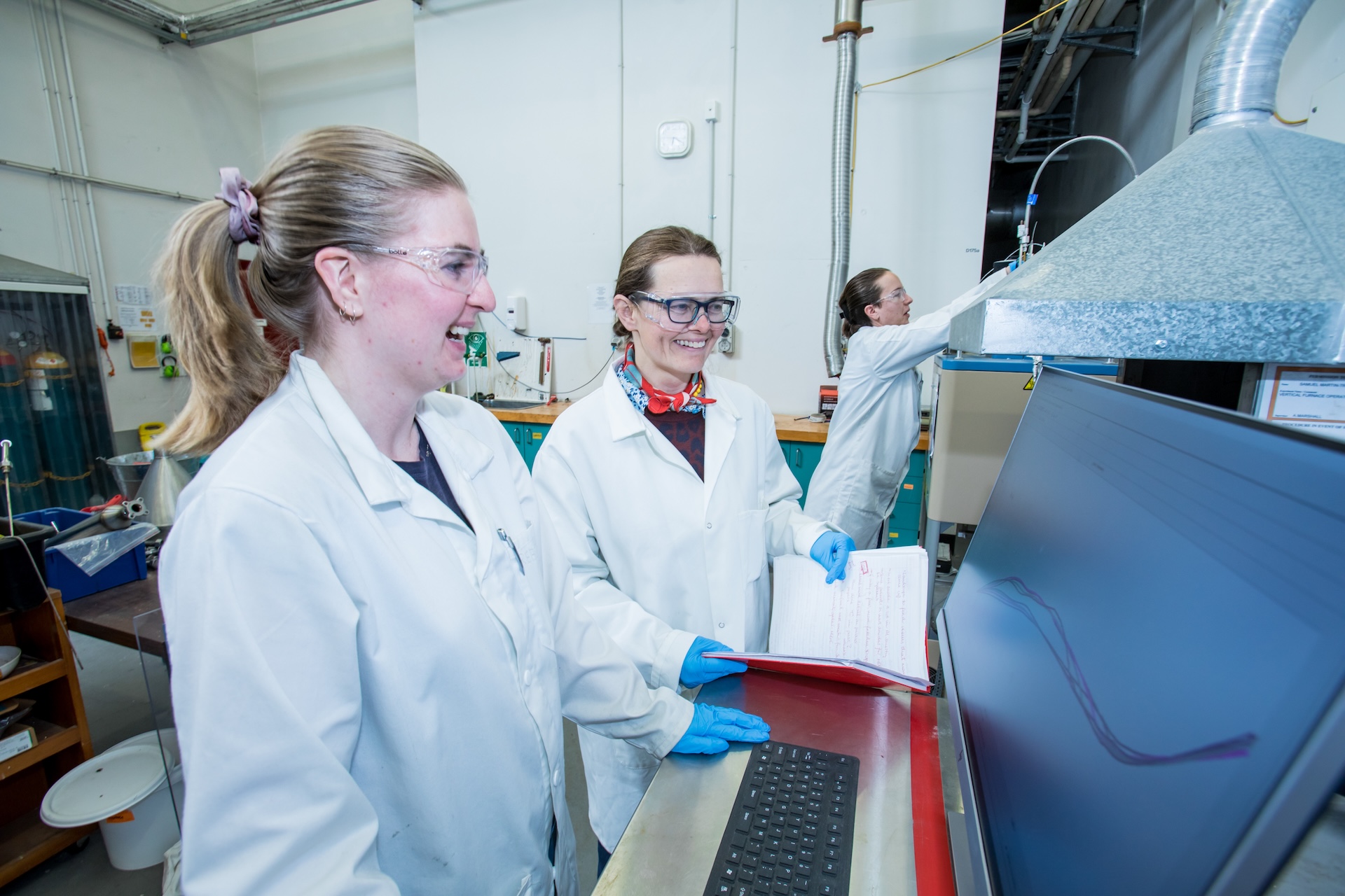Two researchers wearing safety glasses and lab coats looking at a 3D model on a screen in a laboratory.