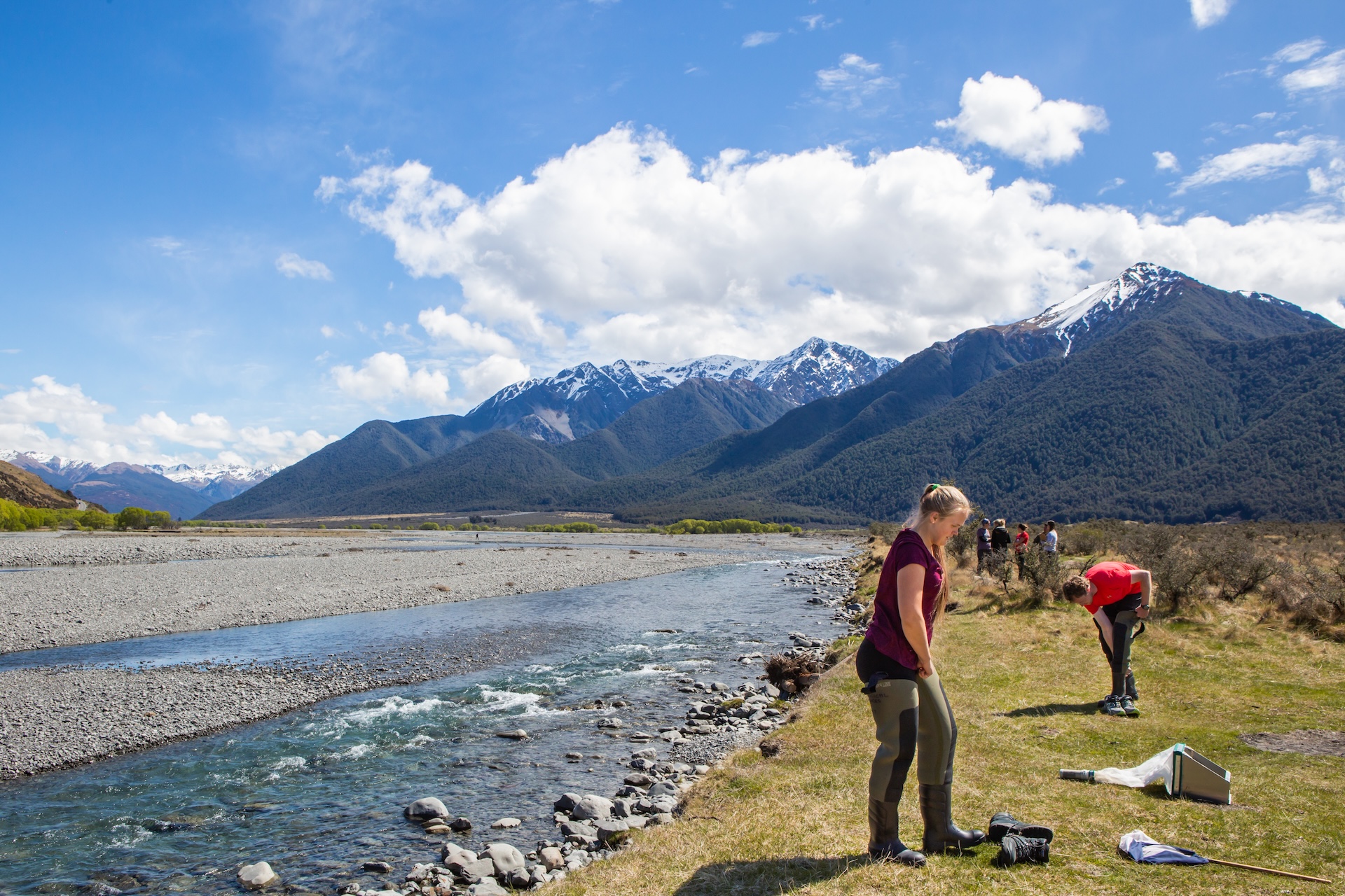 Researchers with waders and nets standing next to a river