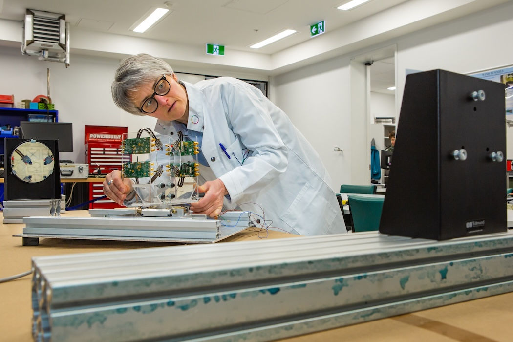 Stefanie Gutschmidt in a lab coat leaning over, and working with, sound detection equipment