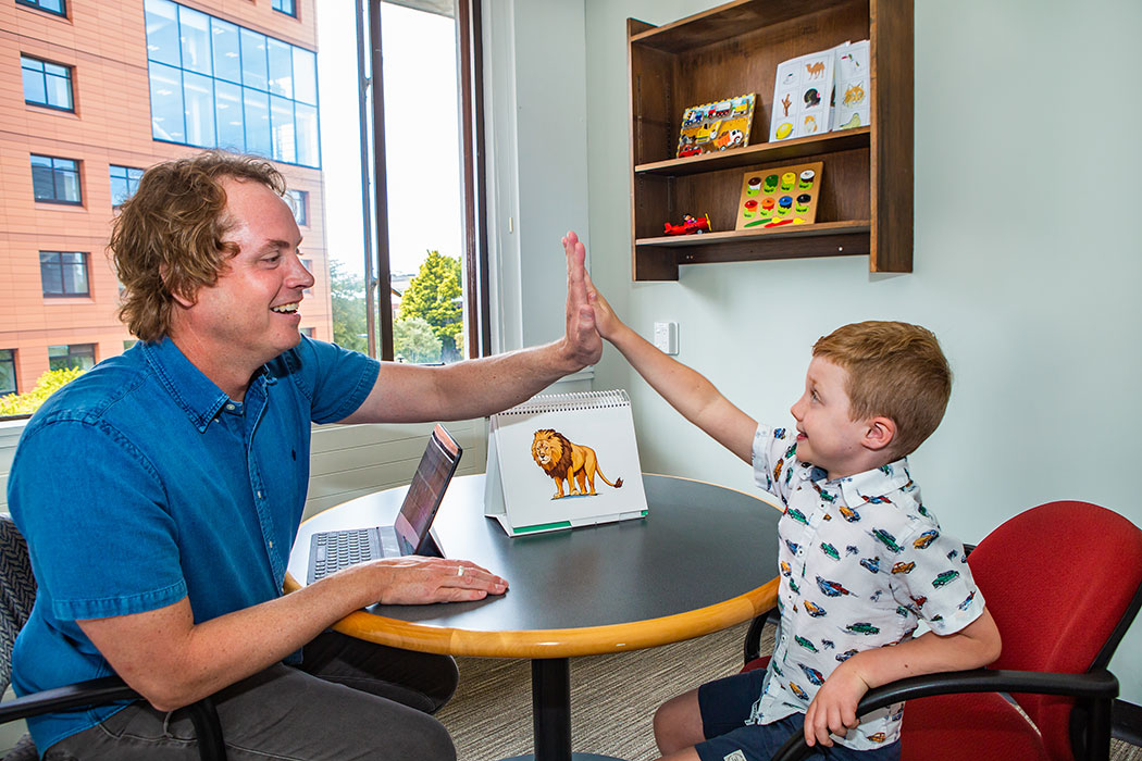 Person sitting at a table with a laptop and giving a child a high-five.