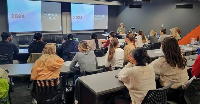 A classroom of UC Online nursing students watch a presentation titled ‘Welcome to HLTH465.’