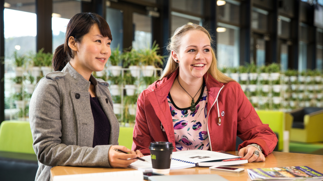 Two teachers sit at a coffee table in a bright and relaxed educational space, learning about new AI tools for educators.