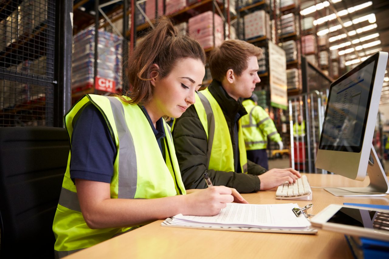 Students in high vis vests stiting at a desk writing in front of computer screens