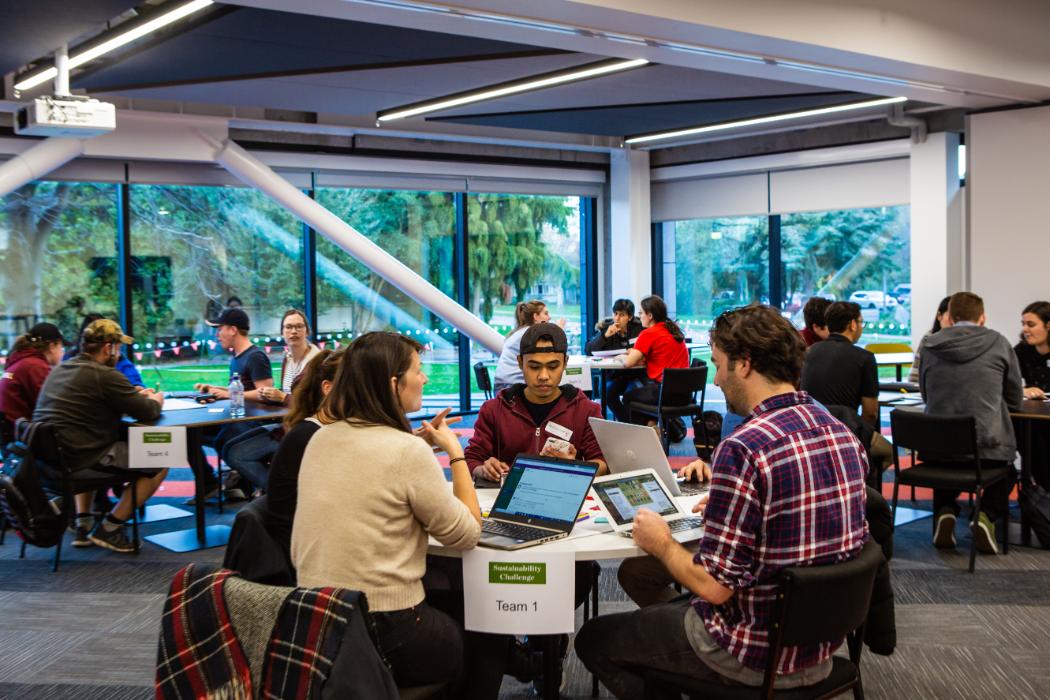 Students sitting in groups around tables working on sustainability posters.