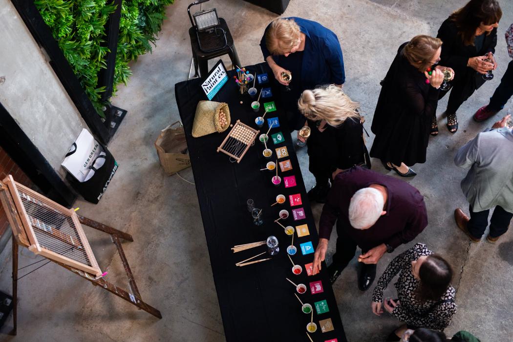 Birds-eye view of a booth at an SDG event with people examining cups filled with coloured sand representing the SDG icon colours.