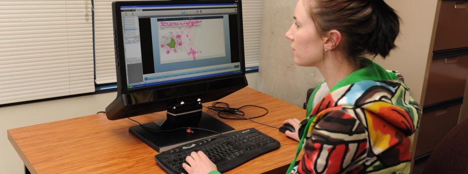 A female member of the stroke rehab team with tie-back brown hair and wearing a colourful top working on a computer