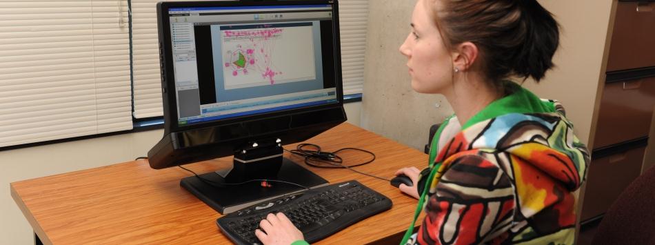 A female member of the stroke rehab team with tie-back brown hair and wearing a colourful top working on a computer