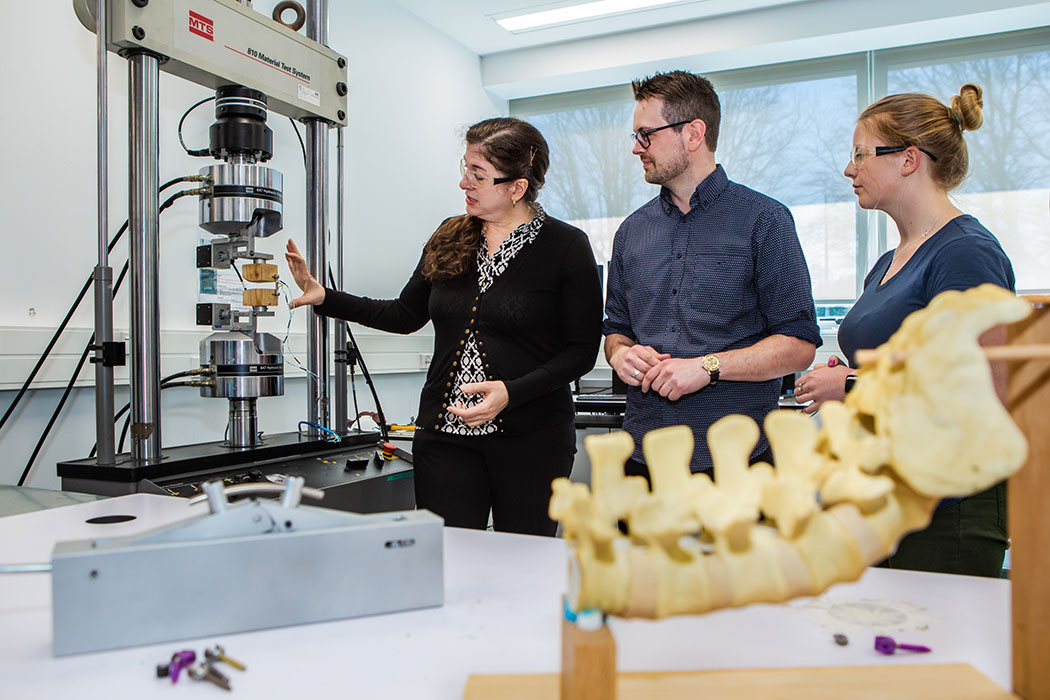 UC researcher Deb Munro demonstrating to two other people with a Material Test System machine.
