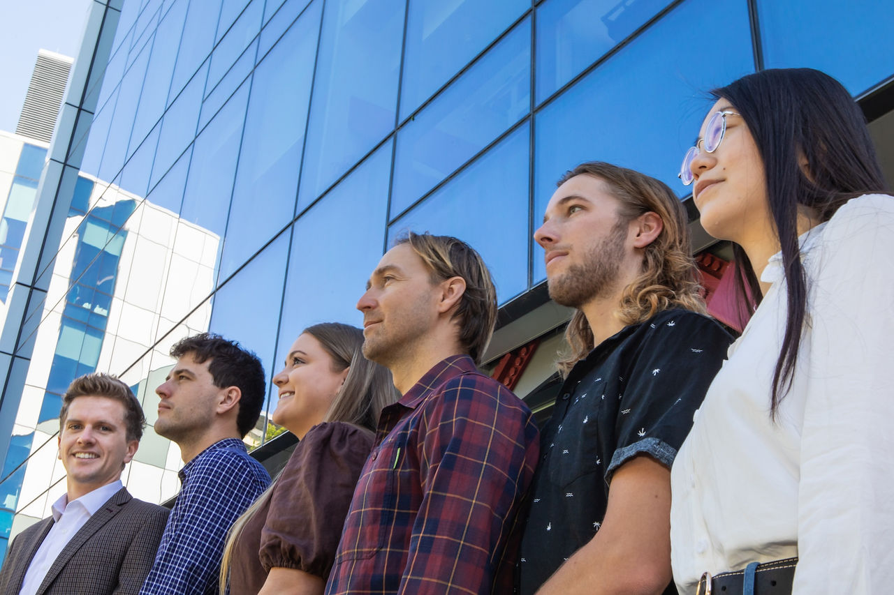 Six reward recipients lined up in front of a glass building  