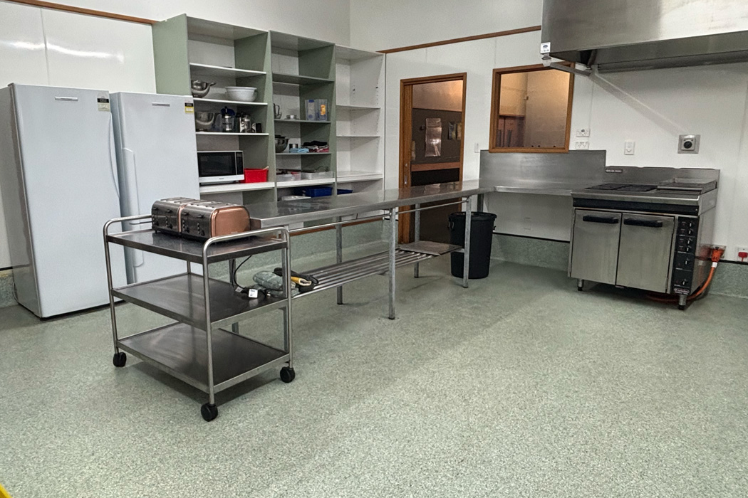 Utility kitchen space with two fridges, a stove, and shelving benches in the middle of the room.