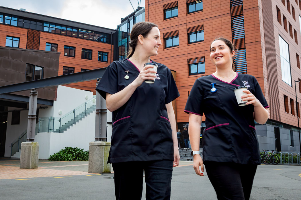 Two UC nursing students in scrubs walking outside of the Rehua building on campus.
