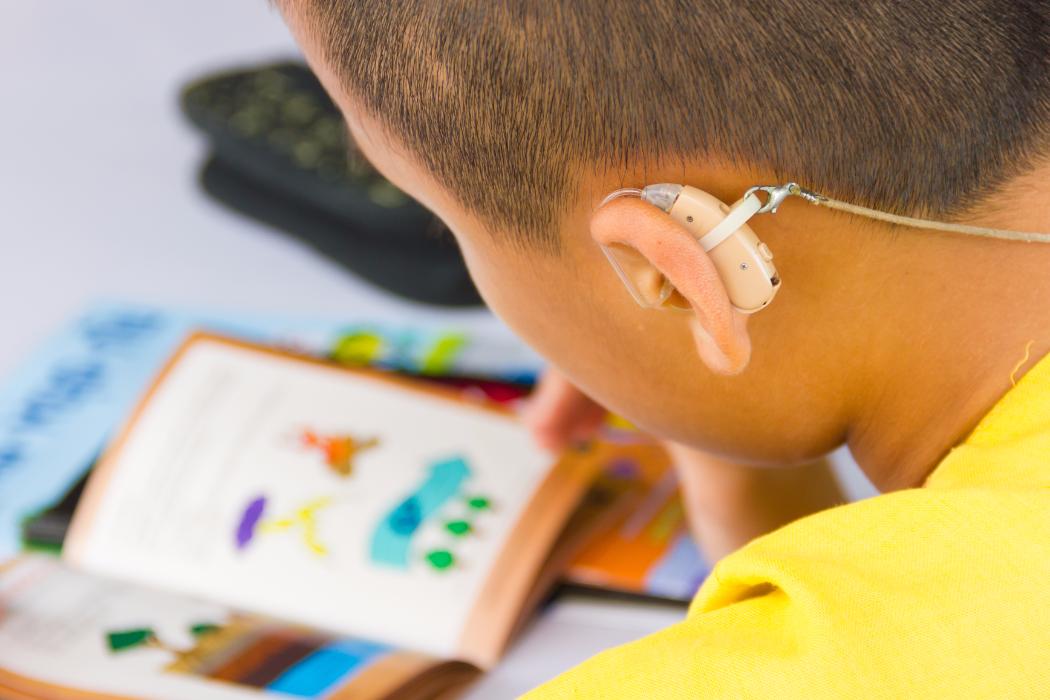 Master of Specialist Teaching Child with Hearing Aid Reading Book