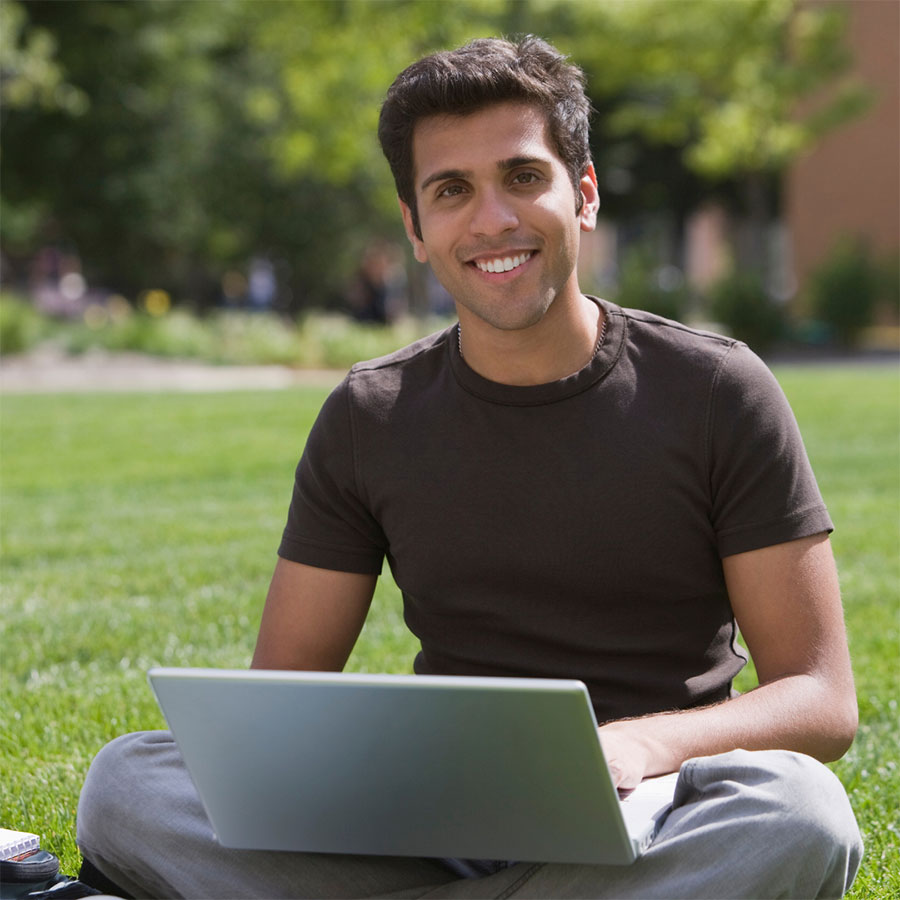 Student sitting cross-legged on a lawn with a laptop.