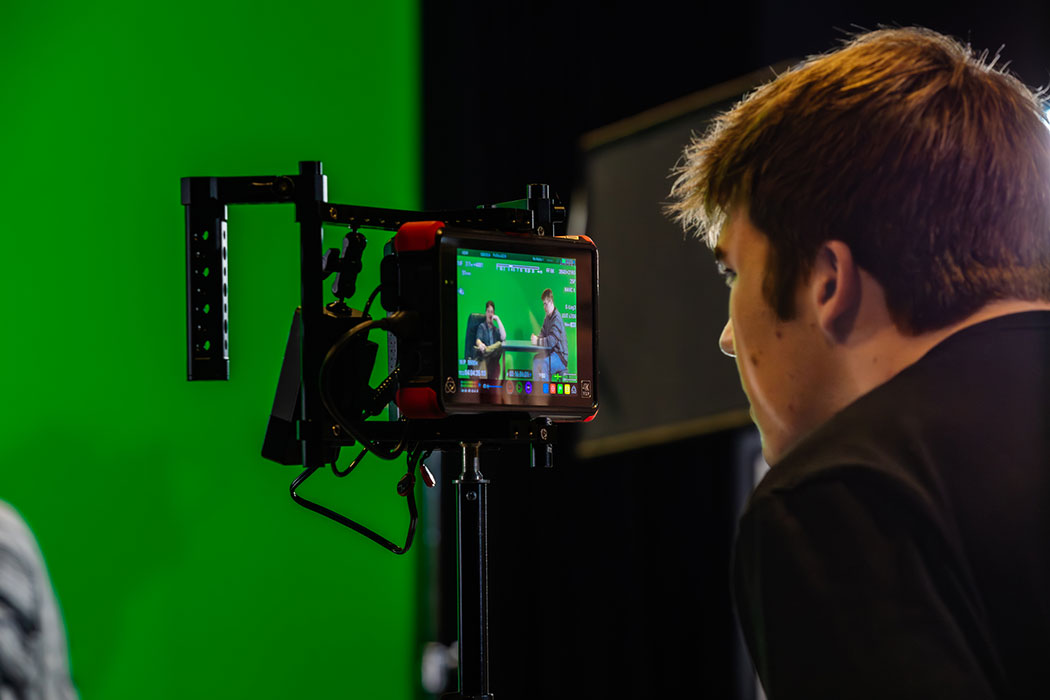 UC student looking through a camera monitor at UC's green screen filming stage.
